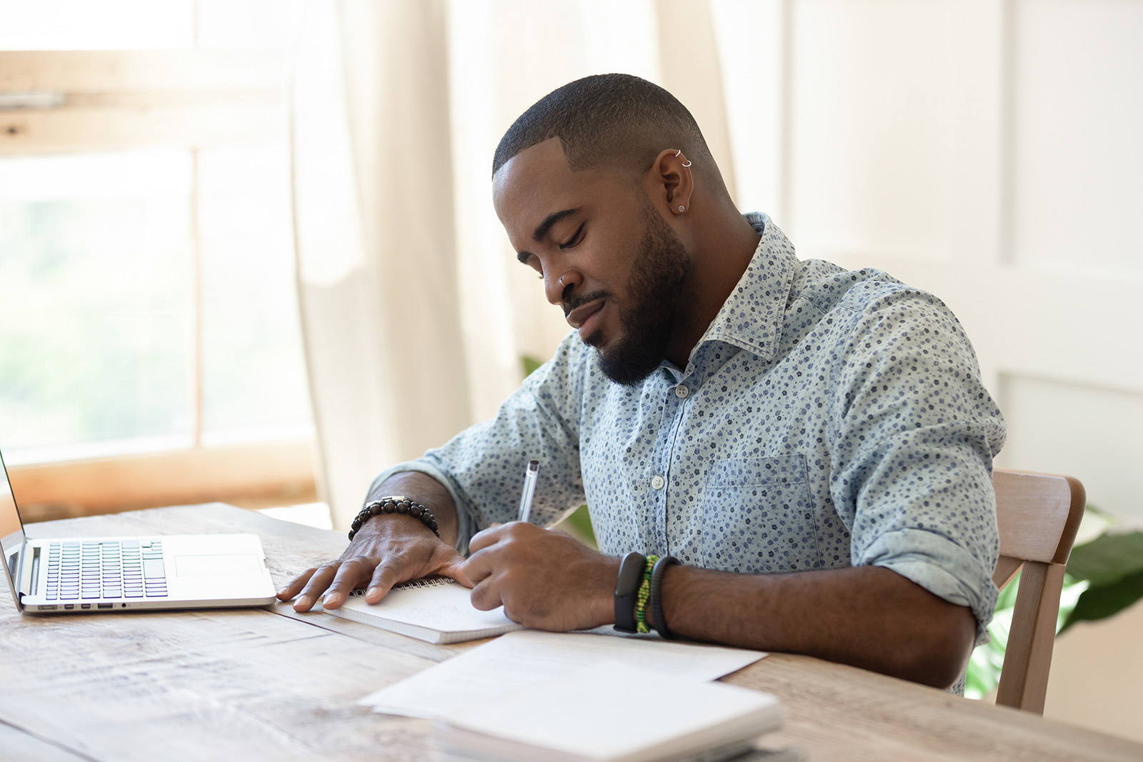 Focused african american man student freelancer making notes studying working with laptop