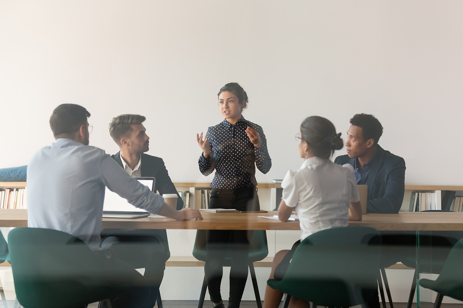 Serious female indian manager talk at diverse group meeting consult clients in boardroom behind glass door